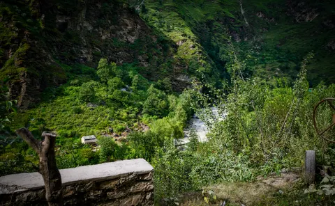 The same view down to the gorge and its river, a concrete topped stone parapet and a cut tree stump filling the lower left and a rusted iron wheel at the right edge.