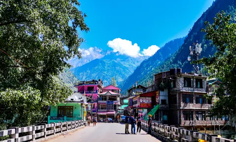 A wide crop of the same street into town, the pink and green buildings at the centre, a phone mast on a roof at the right and cloud sitting on the peak behind.