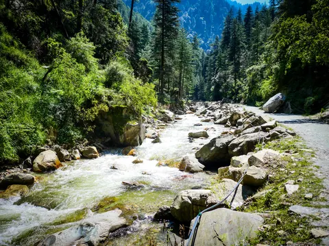 The same stream and track framed a little wider, a big boulder at the right where the track bends and forested ridges stacked behind.