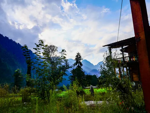 The valley and cloud from the same spot with more of the guesthouse in the frame, its posts and painted balcony at the right and someone crossing the grass below.