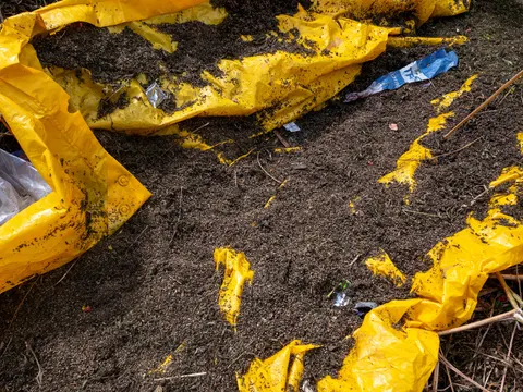 Open yellow plastic sacks and dark material spread on bare ground.
