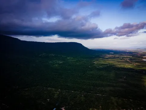 A forested escarpment falling away to farmland on the plain, storm cloud lying low along the ridge.