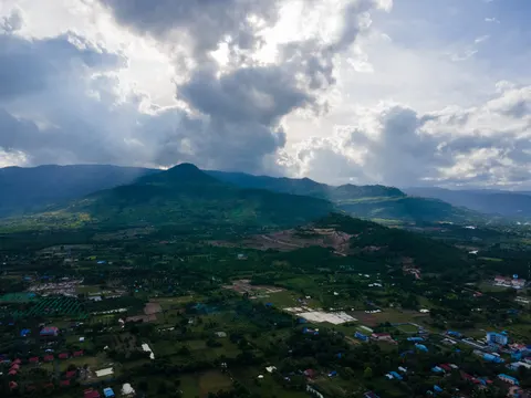 A farmed plain running to a long mountain ridge, sunbeams coming through broken cloud.