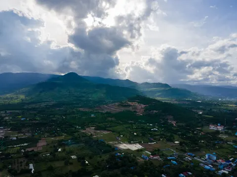 The same plain and ridge, houses and small fields in the foreground under a bright broken sky.