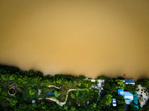 A silted river running past riverside houses and gardens, seen from directly above.