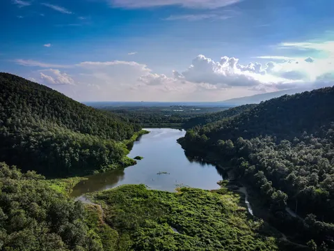 A reservoir lying in the trough between two forested ridges, the plain beyond it.